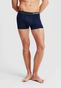 Donje rublje bokserice tamnoplavih s glatkim materijalom, elastični pojas s oznakom "KARL LAGERFELD", kroj koji prianja i kratka duljina nogavica.