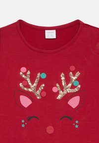 Rde majice iz bombaža s prazničnim dizajnom jelena, ki ima paščke okrašene s svetlečimi sekvini ter pisane pom-pome v roza, turkiznih in zlatih odtenkih.