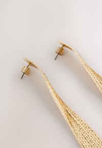 Gold-tone earrings with a wavy shape, featuring a textured surface and a cylindrical stud backing. Smooth texture with a reflective finish.