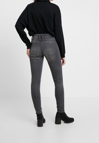 Jeans ajustados grises de cintura alta, con bolsillos traseros, un ligero desgaste y un corte entallado, combinados con una blusa negra de corte suelto y botas negras de tobillo.