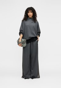 Γκρι φαρδιά φούτερ και παντελόνια με φαρδιά μπατζάκια από απαλό ύφασμα, συνδυασμένα με τσαντάκι φάκελο με εμπριμέ σχέδιο σε πράσινο και γκρι χρώμα.