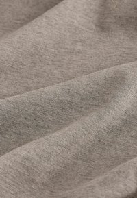 Gros plan sur un tissu doux de couleur marron clair avec une texture de tissage visible et de légers plis créant des ombres et de la profondeur.