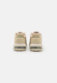 Beige athletic shoes with a mesh upper, cushioned sole, and transparent air unit, featuring a subtle logo on the back.