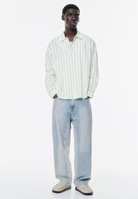 Weiß gestreiftes Langarmshirt mit lässiger Passform, kombiniert mit hellblauen, locker sitzenden Jeans und cremefarbenen Slipschuhen.