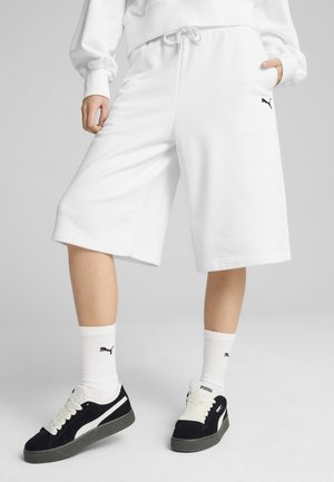 Pantaloni corti bianchi in felpa con vita elastica e cordino, con dettagli del logo nero. Abbinati a scarpe da ginnastica nere e calzini bianchi.