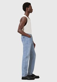 Jeans in denim azzurro chiaro con una vestibilità rilassata, due tasche laterali e dettagli cuciti, abbinati a una maglietta senza maniche bianca. Scarpe nere.