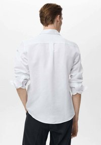 White linen long-sleeve shirt with a classic collar, rolled-up cuffs, and yoke detailing at the back, designed for a relaxed fit.