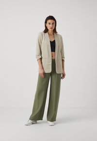 Blazer en lin beige avec des manches roulées, crop top noir et pantalon olive décontracté. Porté avec des baskets blanches.