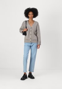 Pelēks adīts kardigāns ar V-veida kaklu, lieliem pogām un frontālām kabatām, kombinēts ar gaiši ziliem taisnā piegriezuma džinsiem un melniem slip-on apaviem.