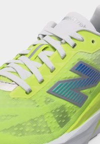 Fel geelgroene sportschoen met witte veters, reflecterende strip en een groot blauwgrijs logo aan de zijkant.