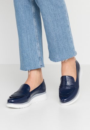 Navy blue patent slip-on shoes with fringe detail and a white sole. Textured finish with a rounded toe and slight heel.