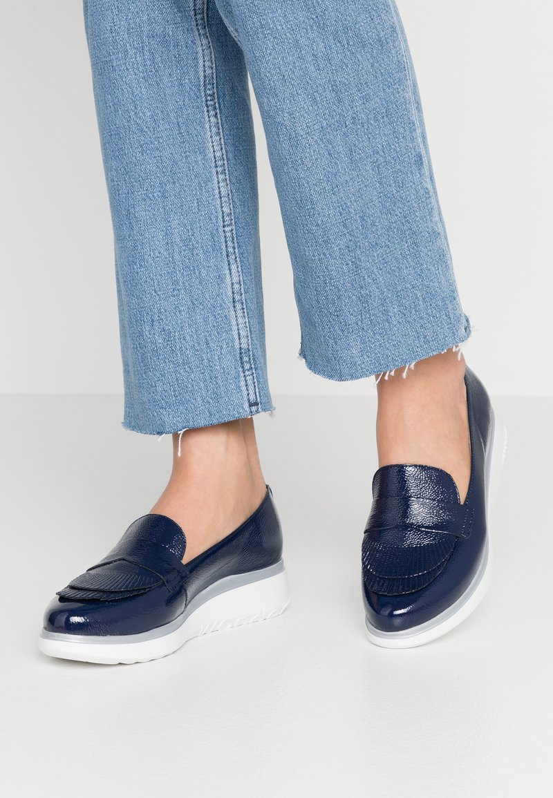 Chaussures à enfiler en cuir verni bleu marine avec détail de franges et semelle blanche. Finition texturée avec un bout arrondi et un petit talon.