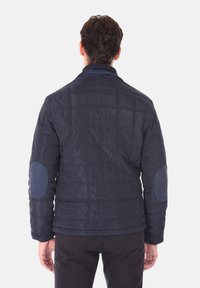 Giacca trapuntata blu navy con colletto alto e toppe sui gomiti in un materiale blu a contrasto, caratterizzata da una texture liscia e un design aderente.