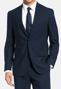 Costume bleu marine avec fermeture à deux boutons, revers crantés et deux poches frontales. Chemise habillée blanche éclatante et cravate sombre texturée à pois.