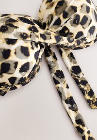 Haut de bikini imprimé léopard avec bonnets rembourrés et liens ajustables sur fond clair.