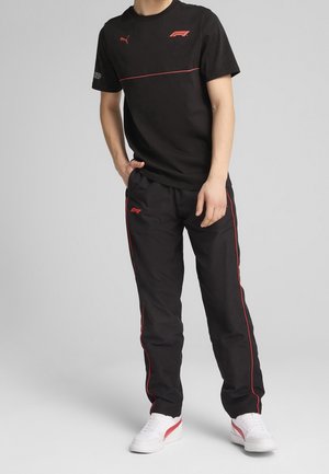 Zwart katoenen T-shirt met rode accenten en logo, gecombineerd met zwarte broek met rode zijkstrepen. Witte sneakers met rode details maken de look compleet.