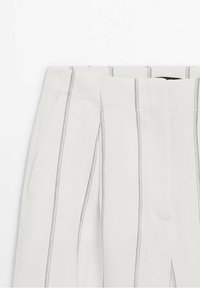 Pantalon gris clair à rayures noires verticales. Il présente un devant plat, des poches latérales et une texture de tissu lisse.