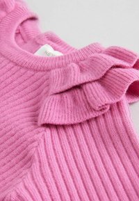 Maglione rosa a coste con un accento arricciato sulla spalla. Il tessuto sembra morbido e lavorato, con un collo rotondo.