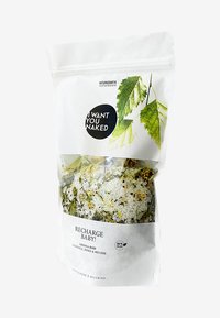 Witte verpakking met bladgraphics, met een doorzichtige venster dat witte badzout toont gemengd met kruiden. Tekst bevat "RECHARGE BABY!" en "100% VEGAN."