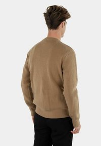 Khaki ribbeltrui met een ronde halslijn en lange mouwen, met een textuurstof en een getailleerde snit. Geen zichtbare logo's of patronen.