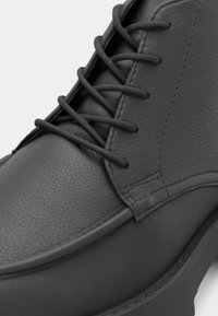 Black leather ankle boot with textured surface, round toe, and matching lace-up design. Features reinforced stitching along the edges.