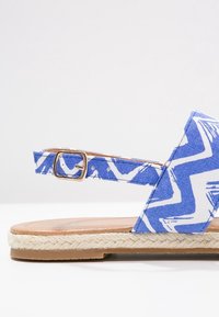 Blåmønstret espadrille sandal med overdel i stof, vævet jute-sål og justerbar ankelrem med en spænde i guldton.
