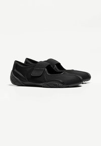 Pantofi sport negri cu o parte superioară din plasă, curea cu arici, design aerodinamic și talpă din cauciuc texturat pentru aderență și flexibilitate.