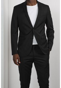 Blazer nero con chiusura a bottone singolo, design slim fit, rever a punta e dettagli discreti sulle tasche, abbinato a una t-shirt bianca.