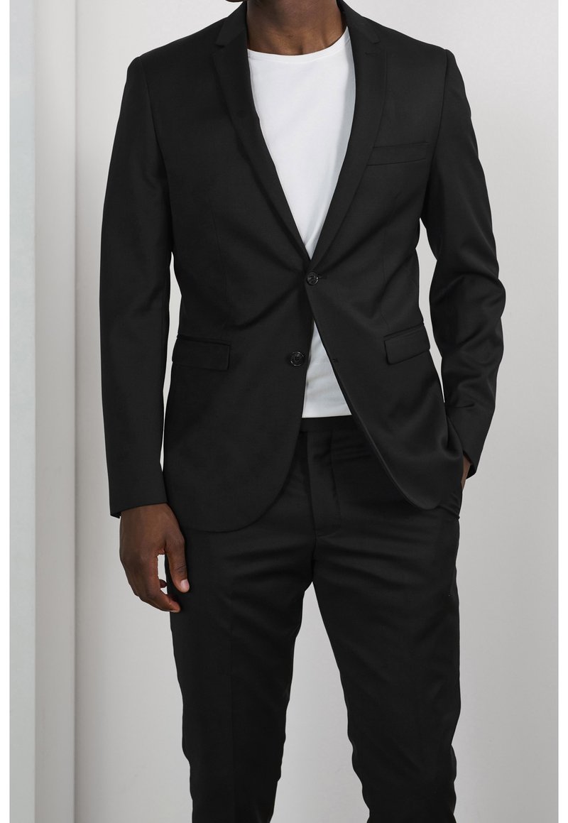 Blazer nero con chiusura a bottone singolo, design slim fit, rever a punta e dettagli discreti sulle tasche, abbinato a una t-shirt bianca.