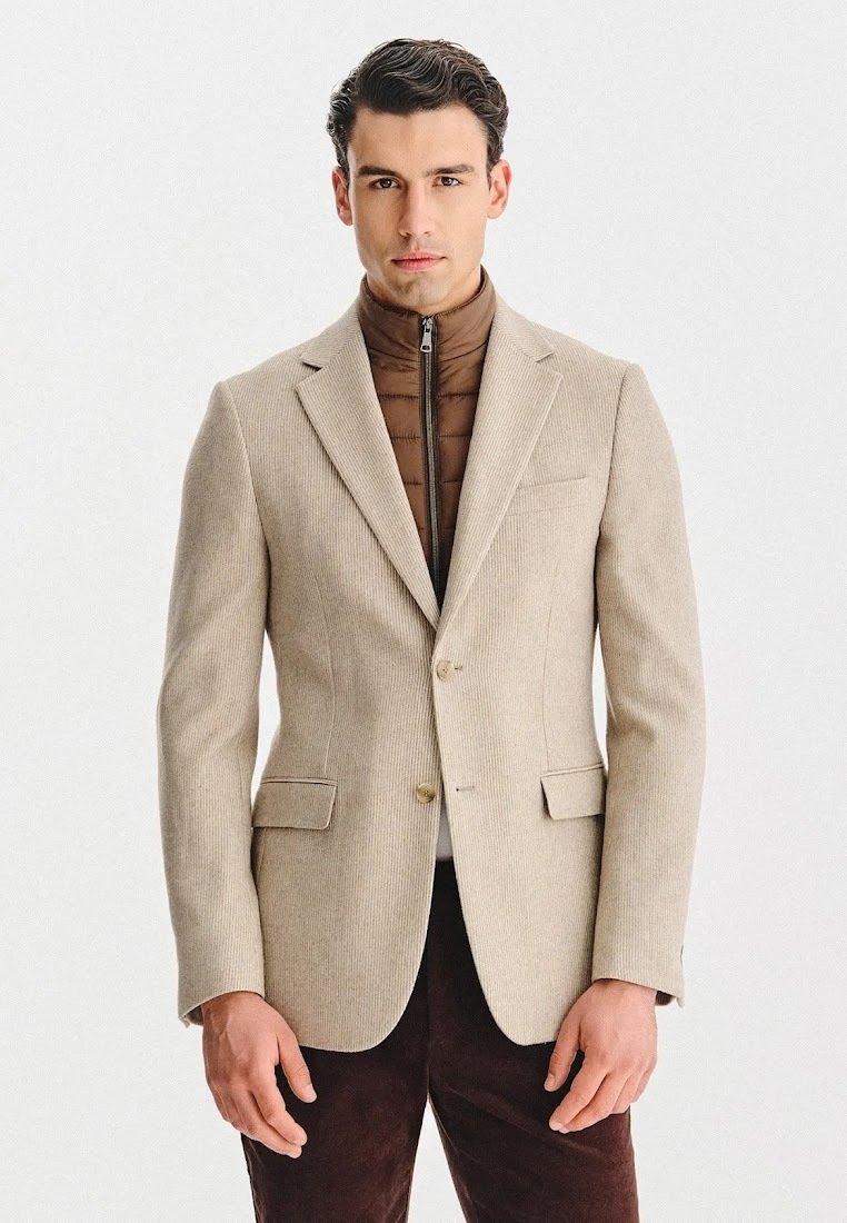 Beżowa żebrowana marynarka z dwoma przednimi kieszeniami, zapinana na jeden guzik; noszona na brązowej pikowanej kurtce z zamkiem; ciemnobrązowe spodnie.