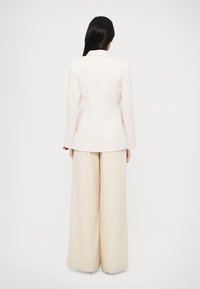 Witte blazer met een getailleerde pasvorm en lange mouwen, gecombineerd met beige broek met wijde pijpen. Minimalistisch ontwerp met strakke lijnen en geen zichtbare accessoires.