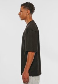 Black cotton t-shirt with short sleeves, a relaxed fit, and a crew neckline. Displayed in profile against a white background.