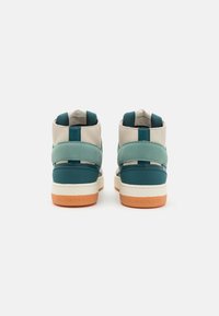 Högskaftade sneakers med en blandning av beige läder och teal mocka, med ljusblå detaljer och en orange gummisula. Märkta med "Calvin Klein Jeans."