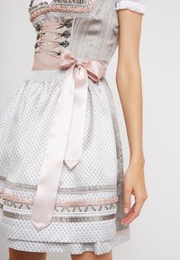 Robe traditionnelle dirndl avec un corsage ajusté, une ceinture en ruban de satin rose et une jupe blanche ornée de motifs floraux et d'accents décoratifs.