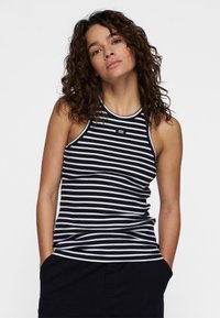 Canotta a righe bianco e nero con un design aderente, realizzata in tessuto elasticizzato. Presenta un collo rotondo e un piccolo logo sul petto.
