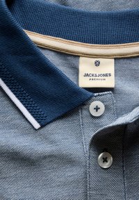 Polo bleu texturé avec col bleu foncé, liseré blanc, deux boutons blancs et étiquette Jack & Jones Premium au niveau du col.