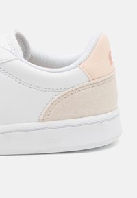 Fehér sneaker sima bőr felülettel, világos rózsaszín velúr sarokrésszel és fehér gumitalppal, finom varrási részletekkel.