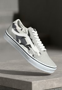 Lace-up sneakers in white and gray, featuring a patterned knitted upper, white rubber sole, and side logo accent. Textured surface detail visible.