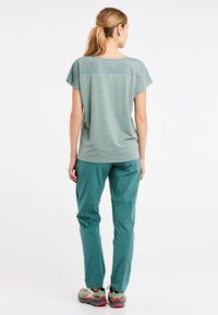 Lichtgroen, T-shirt met korte mouwen en een textuurdesign. Gekoppeld met teal buitenbroeken en sportieve groene sneakers.