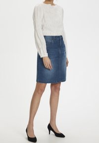 Vit långärmad blus med strukturerad detalj, matchad med en blå jeanskjol i knälängd. Svarta högklackade skor fulländar outfiten.