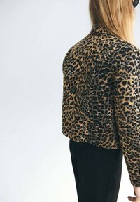 Bunda se zvířecím potiskem s hnědo-černým leopardím vzorem, přizpůsobený střih a texturovaná tkanina. V kombinaci s černými kalhotami.