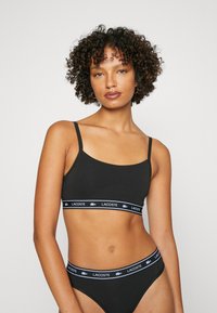 Svart stoff crop topp med tynne stropper, med en logoet elastisk bånd. Kombinert med matchende svart høytlivsundertøy.