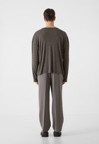Brun-stribet langærmet skjorte med en løs pasform, parret med grå bredbenede bukser og sorte sko. Bagfra ses det afslappede design.