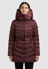 Bordo rdeča puhovka z zategnjenim pasom, visokim ovratnikom in veliko kapuco. Ponaša se z diagonalnim prešitjem in žepi z zadrgo spredaj za funkcionalnost.