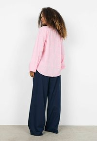 Roze geborduurde blouse met lange mouwen en bloemmotieven; gecombineerd met marineblauwe broek met wijde pijpen. Zacht textiel met een ontspannen pasvorm.