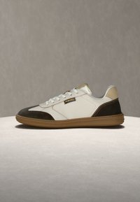 Baskets basses en cuir avec panneaux blanc et marron foncé, talon beige, semelle en gomme, lacets blancs et petite étiquette Versace sur le côté.