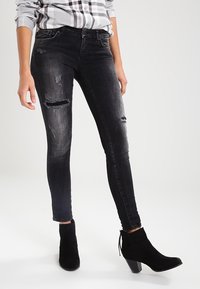 Jean skinny noir avec un design déchiré aux genoux. Fabriqué en denim, il offre une silhouette ajustée et une texture délavée.