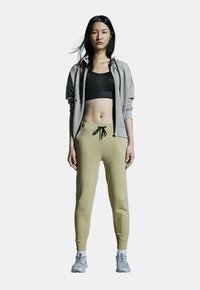 Gray zip-up hoodie, black sports bra, beige sweatpants with drawstring, and gray athletic shoes. Smooth fabric with fitted design.