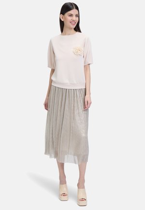 Top rosa chiaro a maniche corte con un dettaglio floreale, abbinato a una gonna midi plissè argento e sandali con zeppa beige. Tessuto di morbida consistenza.