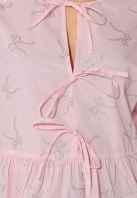 Top rosa chiaro con motivo di fiocchi argentati, scollatura legata, schiena scoperta e orlo arricciato per una maggiore texture e dettaglio.